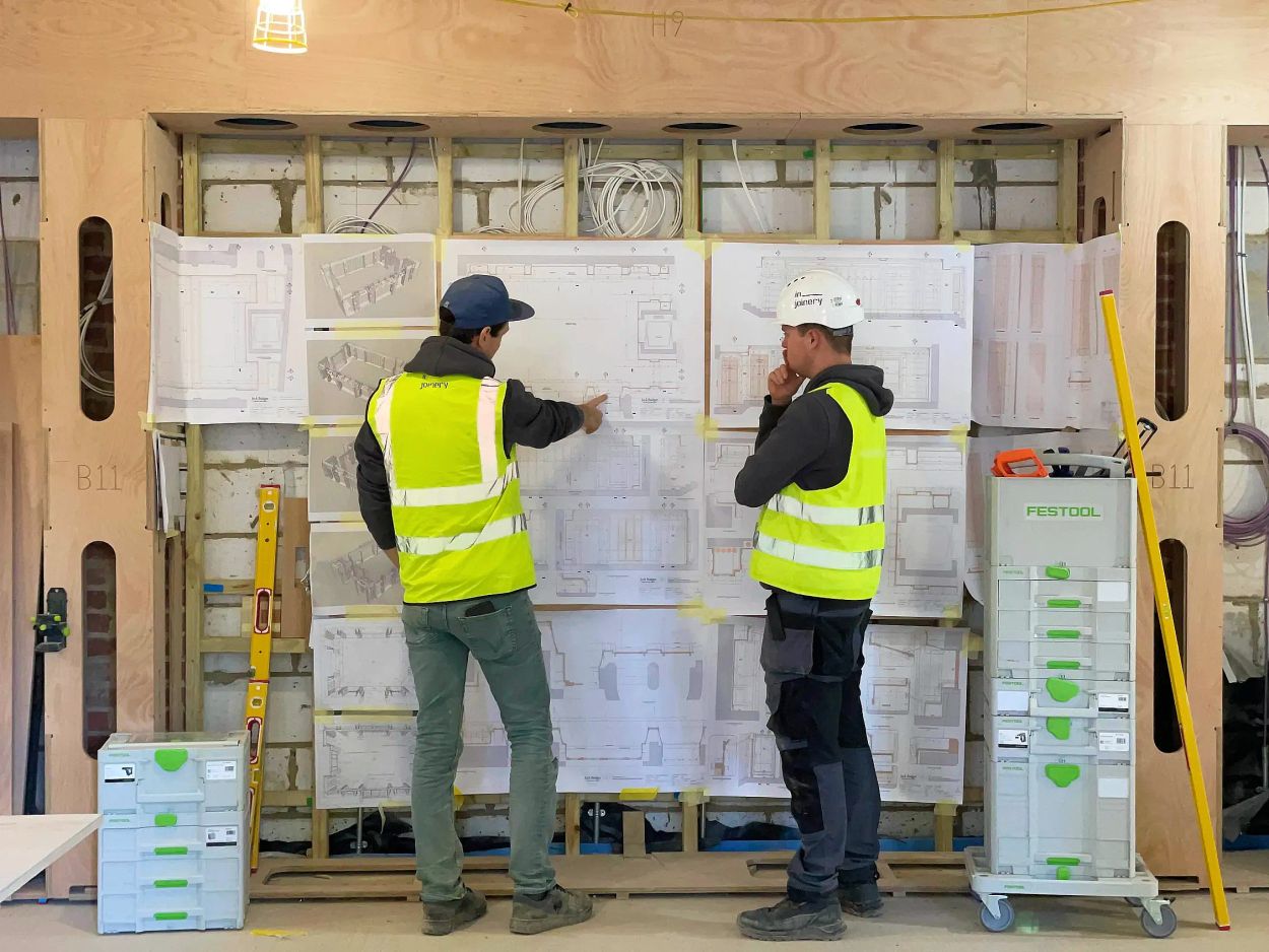 Two professional construction workers in high-visibility jackets and hard hats looking at drawings.